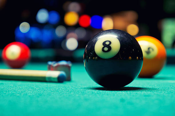 We're your pool table headquarters Close-up picture of an Eight Ball with a cue stick, chalk cube and Five Ball in the background